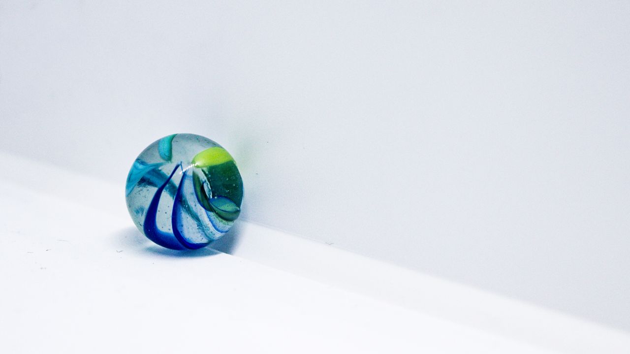 A vivid macro shot of a colorful glass marble against a white background, showcasing simplicity.